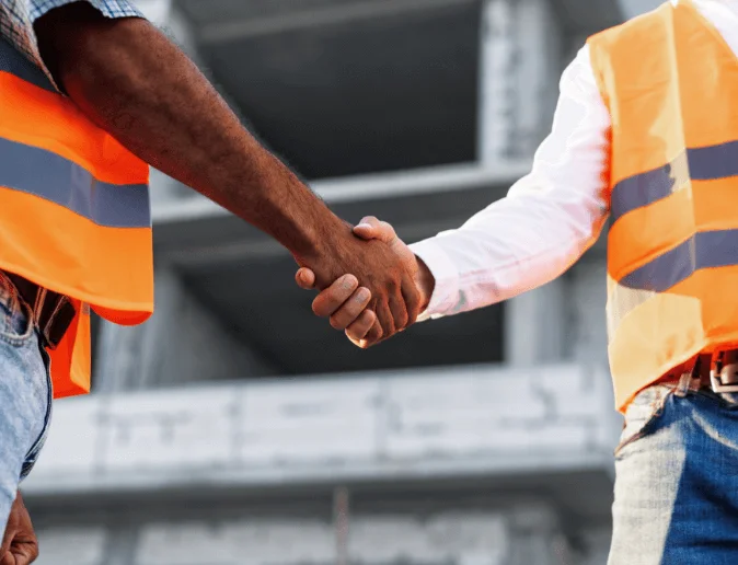 two-men-engineers-workwear-shaking-hands-against-construction-site